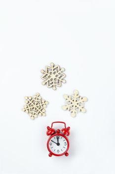 Simple Christmas composition. Small analog red clock, wooden snowflakes on white background. Minimal style flat lay, for social media. Top view. Celebration concept.