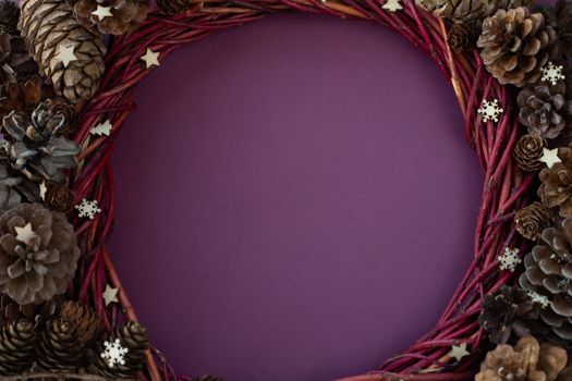 Christmas decorative wreath ivy and various pine fir cedar spruce cones and wooden decor on purple background with copy space for text