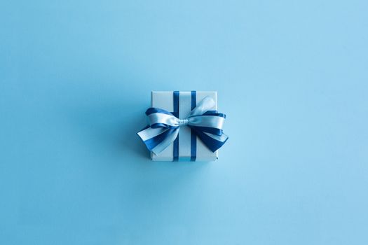 Blue Christmas holiday gift on blue background, small decorated box with ribbon bow