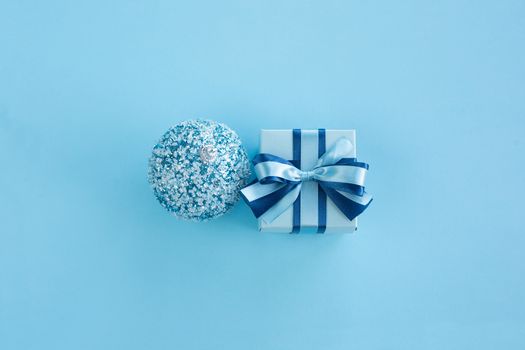 Blue Christmas holiday gift and bauble on blue background, small decorated box with ribbon bow