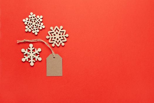 Christmas decoration, three little wooden snowflakes and craft tag on bright red background, copy space. Festive, New Year, sales concept. Horizontal, flat lay. Minimal style. Top view.