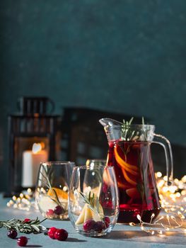 Winter sangria on dark christmas holiday background. Jugful of sangria and glasses with fruit slice, cranberry and rosemary. Copy space for text or design. Vertical.