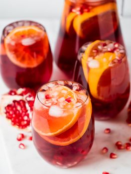 Winter sangria on white marble background. Jugful of sangria and glasses with orange slice and pomegranate. Copy space for text or design. Vertical.