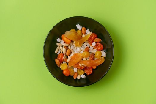 A fresh dried and candied fruits and nuts in black bowl on green bakground. Concept of nutrient and healty breakfast or meal and vegan or vegetarian food.