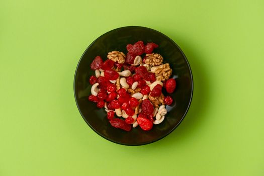 A fresh dried and candied fruits and nuts in black bowl on green bakground. Concept of nutrient and healty breakfast or meal and vegan or vegetarian food.