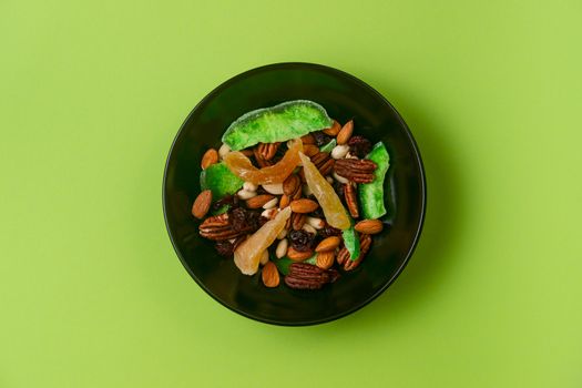 A fresh dried and candied fruits and nuts in black bowl on green bakground. Concept of nutrient and healty breakfast or meal and vegan or vegetarian food.