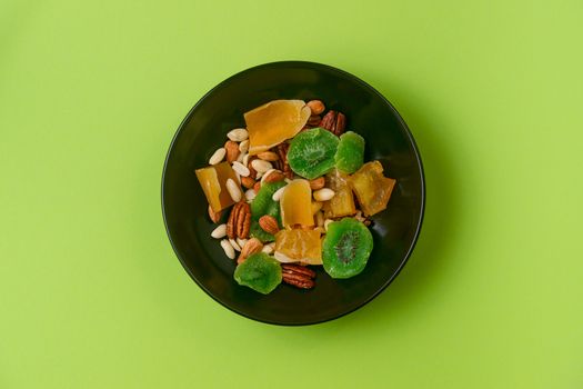 A fresh dried and candied fruits and nuts in black bowl on green bakground. Concept of nutrient and healty breakfast or meal and vegan or vegetarian food.