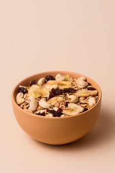 A fresh granola with dried and candied nuts and fruits in beige colour bowl closeup on beige bakground. Concept of nutrient and healty breakfast or meal