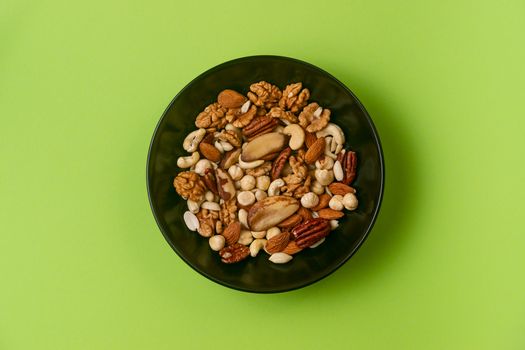 A fresh dried and candied fruits and nuts in black bowl on green bakground. Concept of nutrient and healty breakfast or meal and vegan or vegetarian food.