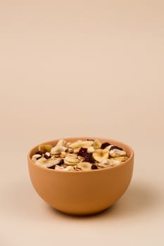 A fresh granola with dried and candied nuts and fruits in beige colour bowl closeup on beige bakground. Concept of nutrient and healty breakfast or meal