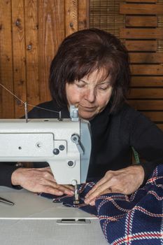 Woman sewing on a sewing machine. Wooden wall