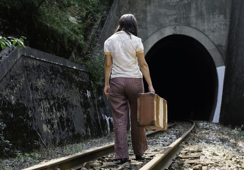 Woman and vintage suitcase on railway road and tunnel. 