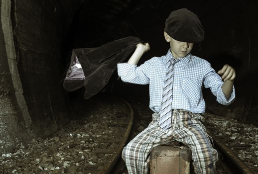 Child in vintage clothes sits on railway road in front of a tunnel.