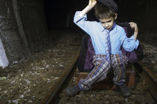 Child in vintage clothes sits on railway road in front of a tunnel.