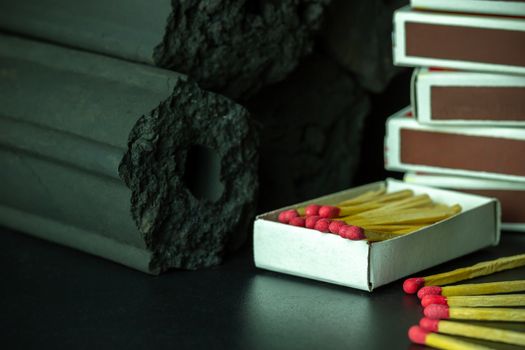 Box of matches and Carbon activated bamboo charcoal on dark background. Concept of fuel for living in the forest. Closeup and copy space.