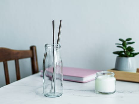 Metal drinking straws in glass bottle on white marble table indoor. Metal straws on table in living room interior. Recyclable straws, zero waste concept.