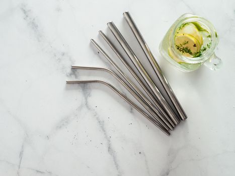 Metal drinking straws and cold drink in glass mason jar on white marble background. Top view or flat lay. Copy space for text or design. Recyclable straws, zero waste concept. Banner.