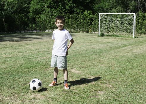 Child playing football in a stadium. Trees on the background