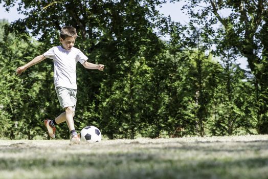 Child playing football in a stadium. Trees on the background