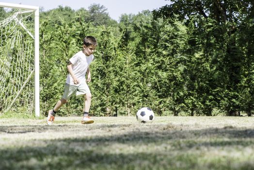 Child playing football in a stadium. Trees on the background