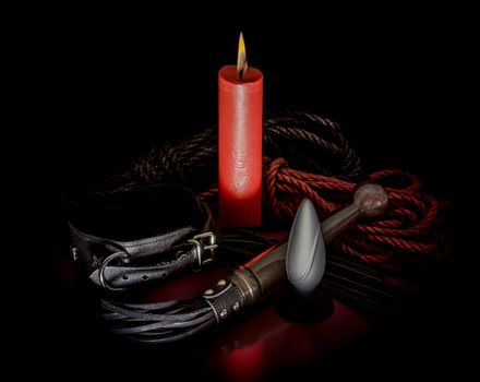bdsm rope with a red burning candle and a lash with a leather collar on a dark background
