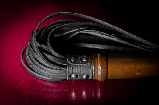 black leather bdsm lash on a red background
