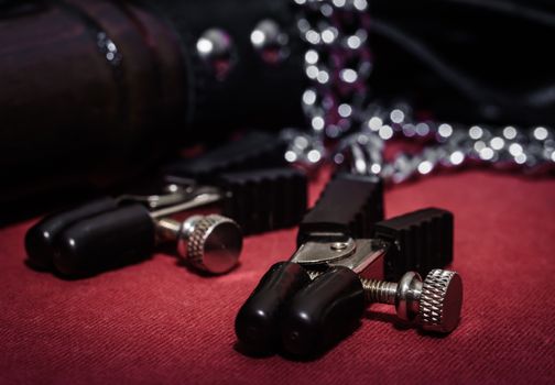 bdsm accessory nipple clasp with metal chain on a red background close-up