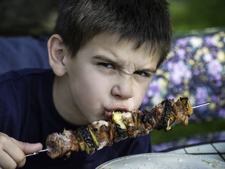 Child eating meat on a skewer. Barbecue meat
