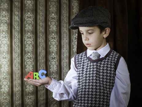 Child in vintage clothes hold multicolor letters a b c