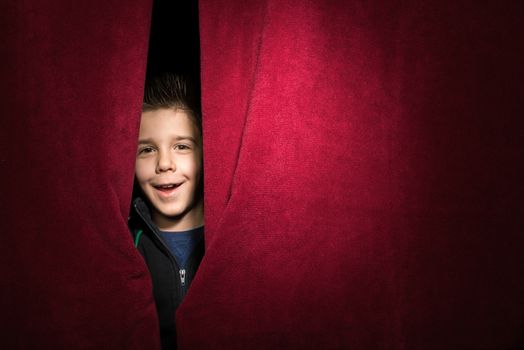 Child appearing beneath the curtain. Red curtain.