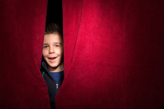 Child appearing beneath the curtain. Red curtain.