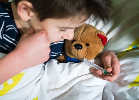 Sick child in bed with teddy bear. Measuring the temperature with a thermometer.