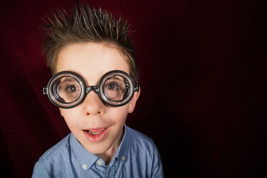 Smiled child with big glasses. Red curtain background