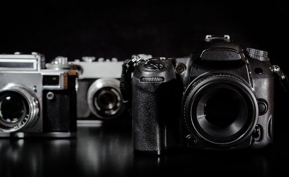 two vintage cameras and one modern camera on a black background closeup