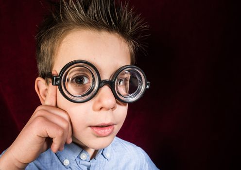 Thinking child with big glasses. Red curtain background