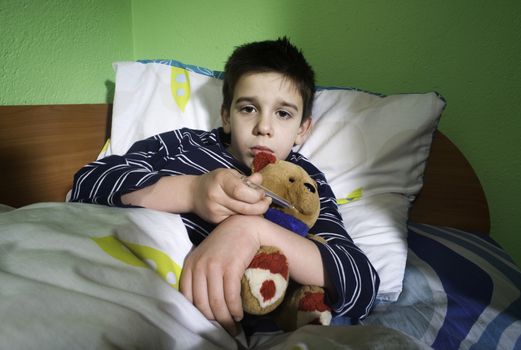 Sick child in bed with teddy bear. Measuring the temperature with a thermometer.