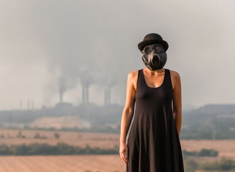 young girl in a black dress and gas mask on the background of smoking factory chimneys in Ukraine