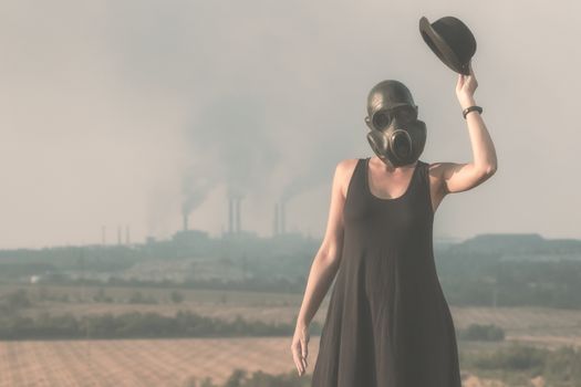 young girl in a black dress and gas mask on the background of smoking factory chimneys in Ukraine