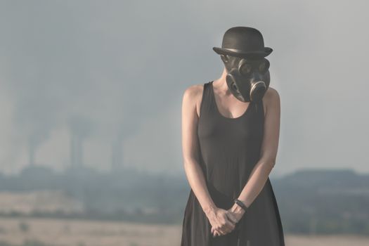young girl in a black dress and gas mask on the background of smoking factory chimneys close up
