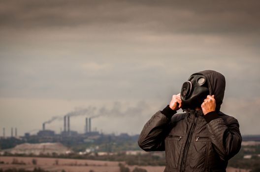 one man in a gas mask and a hood amid smoke from factory pipes close up