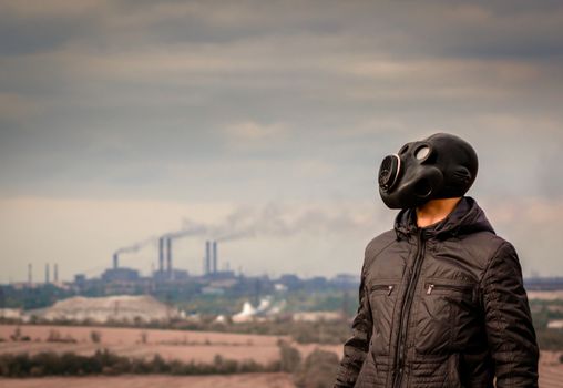man in a gas mask amid smoke from factory pipes close up