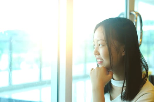 Side view portrait of a young asian girl looking through a window at restaurant