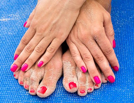 female hands with red manicure on female legs with a red pedicure with sand on legs and hands on a blue yoga mat on the beach