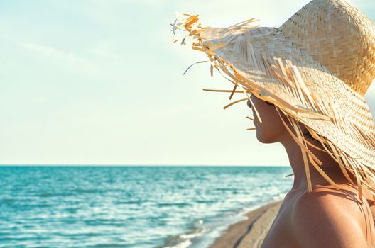 young girl in a straw hat on the background of the surf of the sea and sky with clouds close up