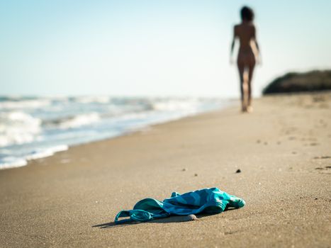 swimsuit in the sand on the beach near the sea surf on the background of a naked female figure and blue sky