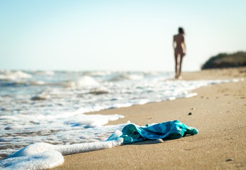 swimsuit in the sand on the beach near the sea surf on the background of a naked female figure and blue sky