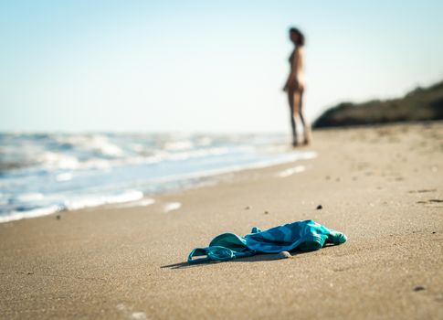 swimsuit in the sand on the beach near the sea surf on the background of a naked female figure and blue sky