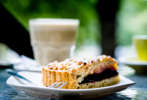triangular piece of poppy pie and a fork with powdered sugar on a background of a transparent glass with white coffee and a yellow cup