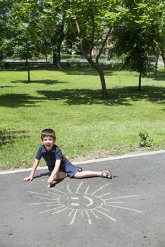 Child drawing sun on asphalt in a park