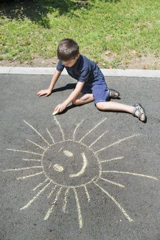 Child drawing sun on asphalt in a park